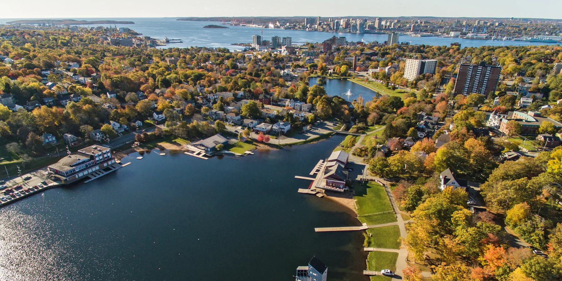 Aerial view over Lake Banook in Dartmouth in autumn, with the Halifax skyline and harbour beyond.